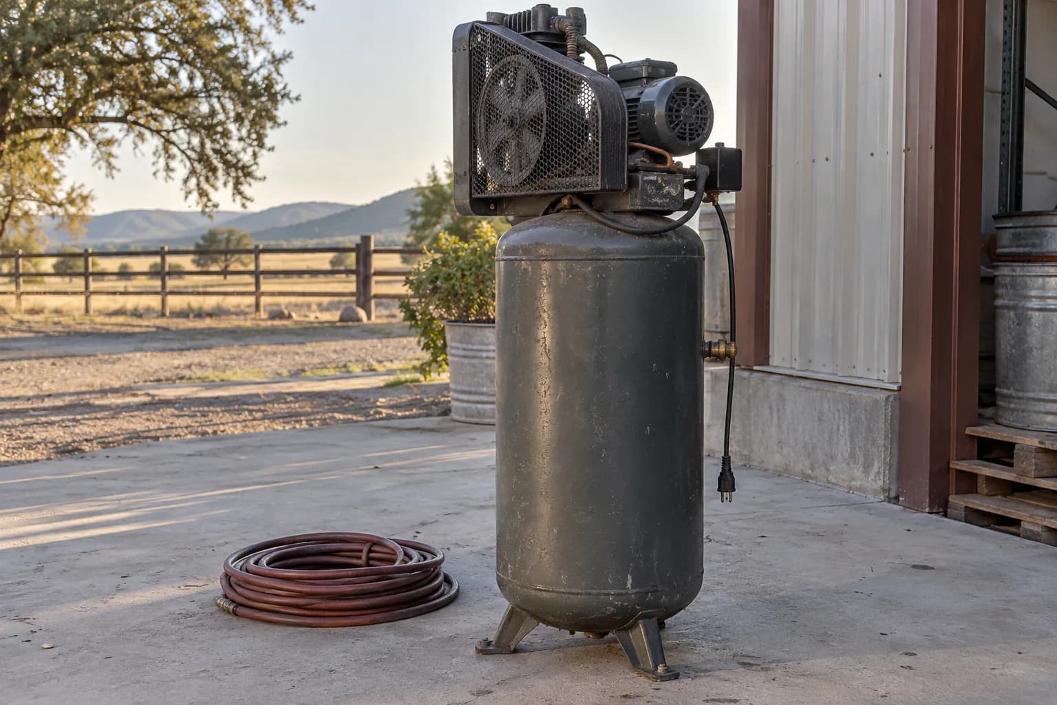 An off vertical air compressor with an intact belt guard and loose air hose on an outdoor concrete pad.